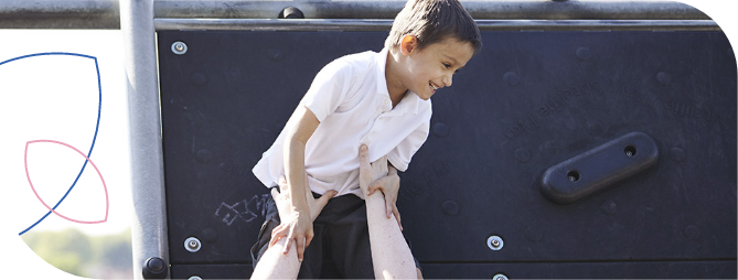 criança sorridente usando camiseta branca sendo apoiada por um adulto enquanto sobe em estrutura de playground