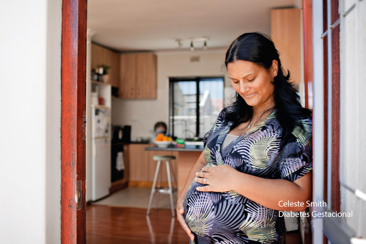 Celeste Smith, paciente com diabetes gestacional, é uma mulher morena, cabelos longos e escuros, pousa encostada em uma porta com vista para uma cozinha