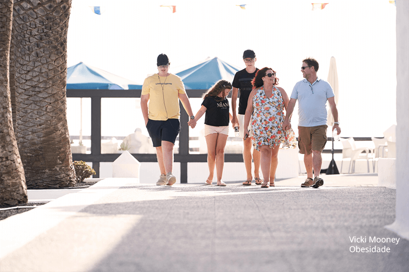 Foto de uma família com sinais de obesidade, pai e mãe e três adolescentes, dois garotos e uma menina, fazendo uma caminhada num resort.
