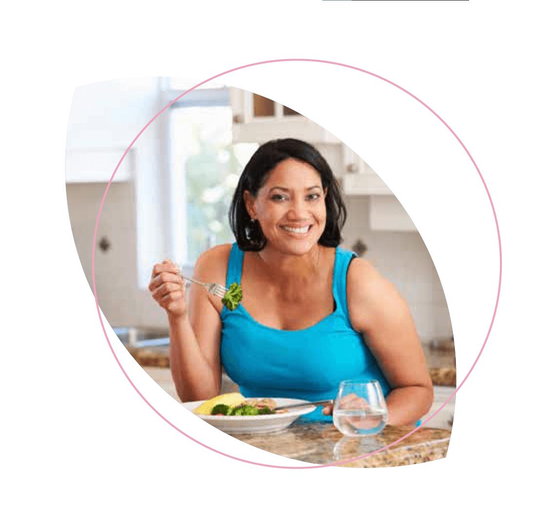 mulher de azul sorrindo com um prato na mesa e um brócolis no garfo